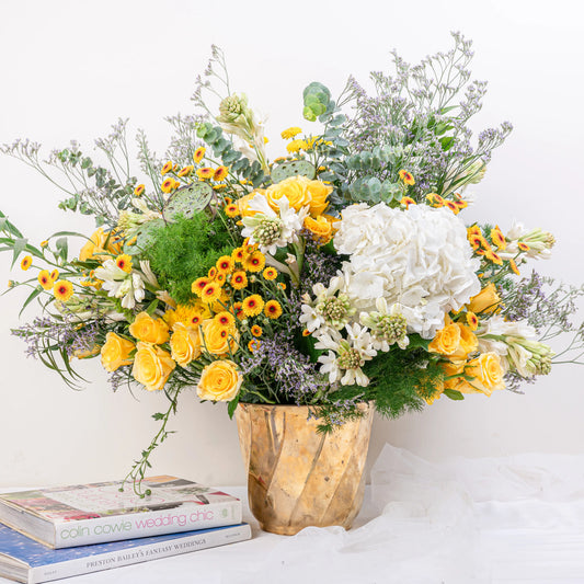 Citrus & Ivory luxury centerpiece with yellow roses, white hydrangea, gerberas, tuberose and eucalyptus in gold geometric vase by House of Mograa